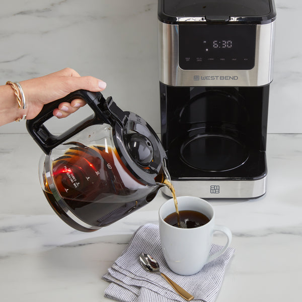 12-cup hot and iced coffee maker with glass carafe pouring coffee, mug on counter