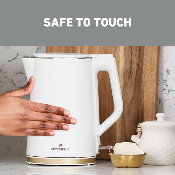 White electric kettle with side handle and gold base trim; hand holding