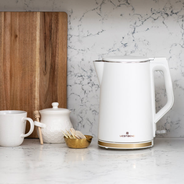 White electric kettle on countertop with gold base ring and side handle