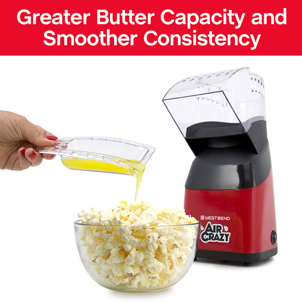 Red air popcorn machine with clear lid open, pouring oil into popcorn bowl
