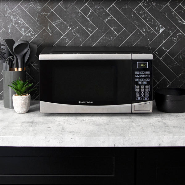 Black microwave oven on countertop with keypad and cooking utensils