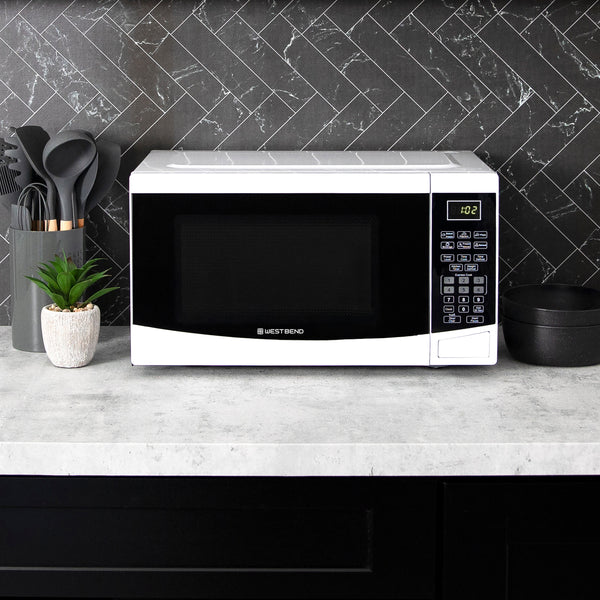 Black microwave oven on countertop with keypad and kitchen tools